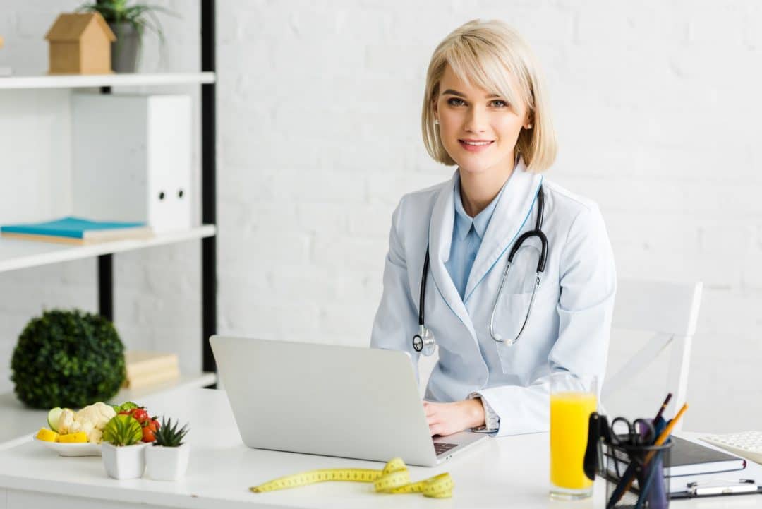 cheerful-blonde-nutritionist-sitting-near-laptop-and-glass-of-fresh-orange-juice.jpg